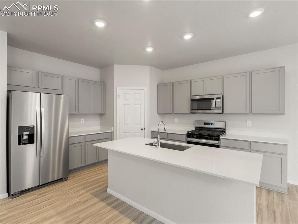 Image 6 of 30: Kitchen with stainless steel appliances, gray cabinetry, an island with sin