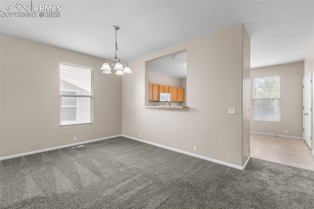 Image 11 of 38: Unfurnished dining area with light carpet and a chandelier