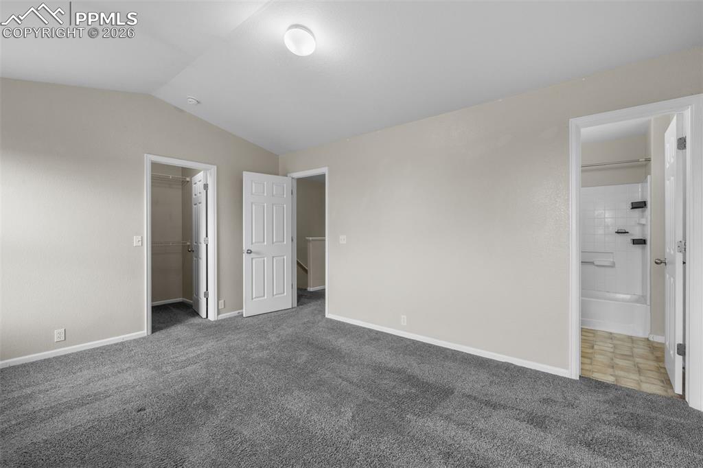 Image 22 of 38: Unfurnished bedroom with carpet, vaulted ceiling, a spacious closet, and en