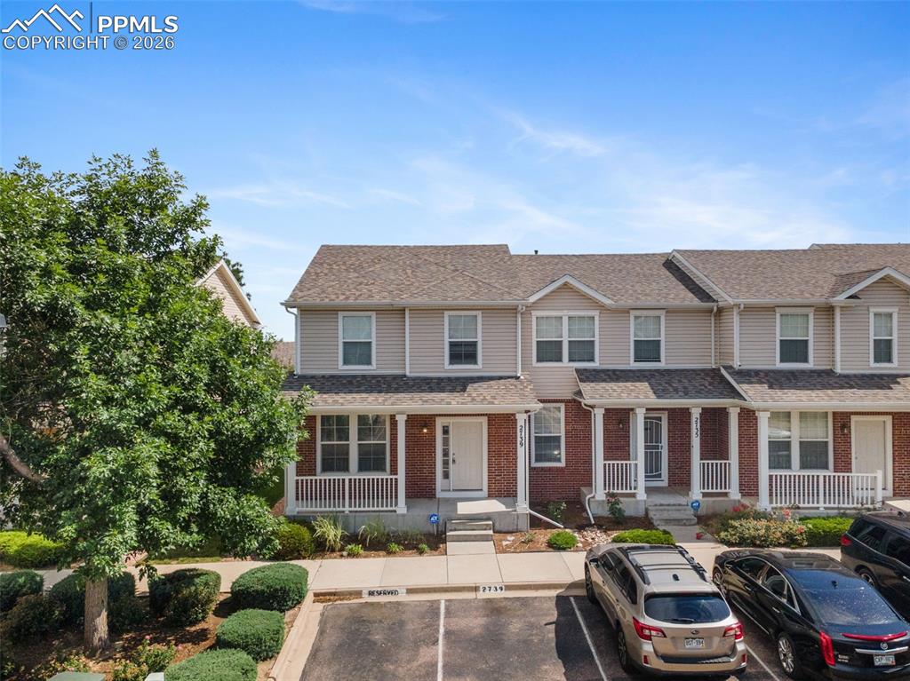 Image 3 of 38: View of front facade with uncovered parking, a porch, brick siding, and a s