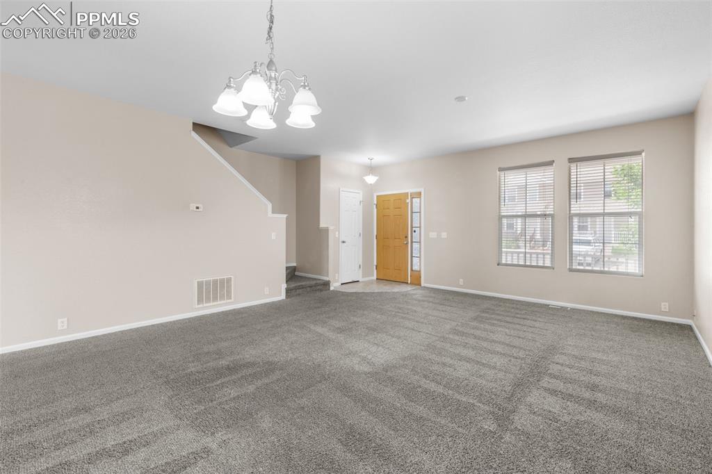 Image 7 of 38: Unfurnished living room with carpet flooring, stairway, and a chandelier