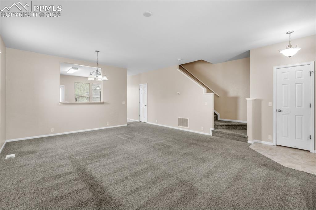 Image 9 of 38: Unfurnished living room with carpet flooring, stairs, and a chandelier
