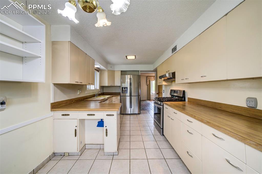 Image 14 of 49: Kitchen with stainless steel appliances, range hood, a chandelier, a sink,