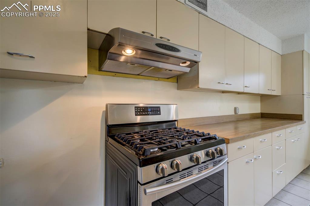 Image 16 of 49: Kitchen with stainless steel gas stove, ventilation hood, light countertops