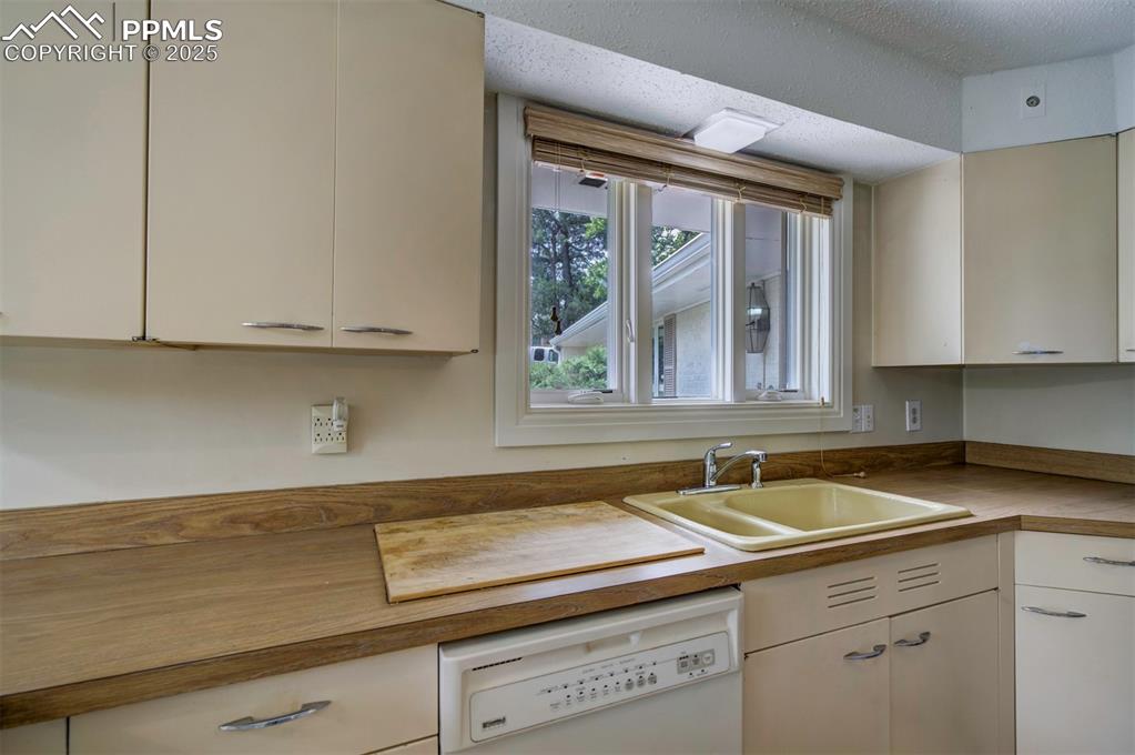 Image 17 of 49: Kitchen with white dishwasher, a sink, white cabinetry, and a textured ceil
