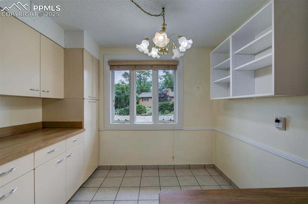 Image 18 of 49: Kitchen with a chandelier, open shelves, light tile patterned flooring, a t