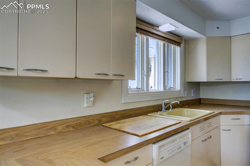 Image 19 of 49: Kitchen with a sink, white dishwasher, white cabinetry, and a textured ceil