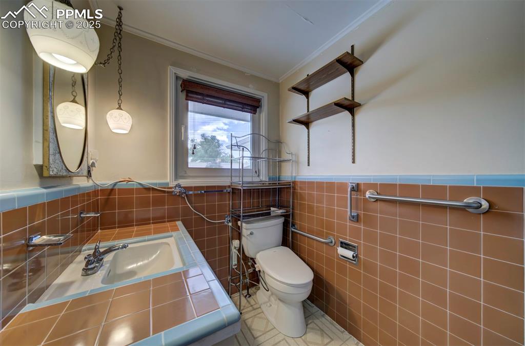 Image 23 of 49: Half bath featuring crown molding, toilet, tile walls, a wainscoted wall, a