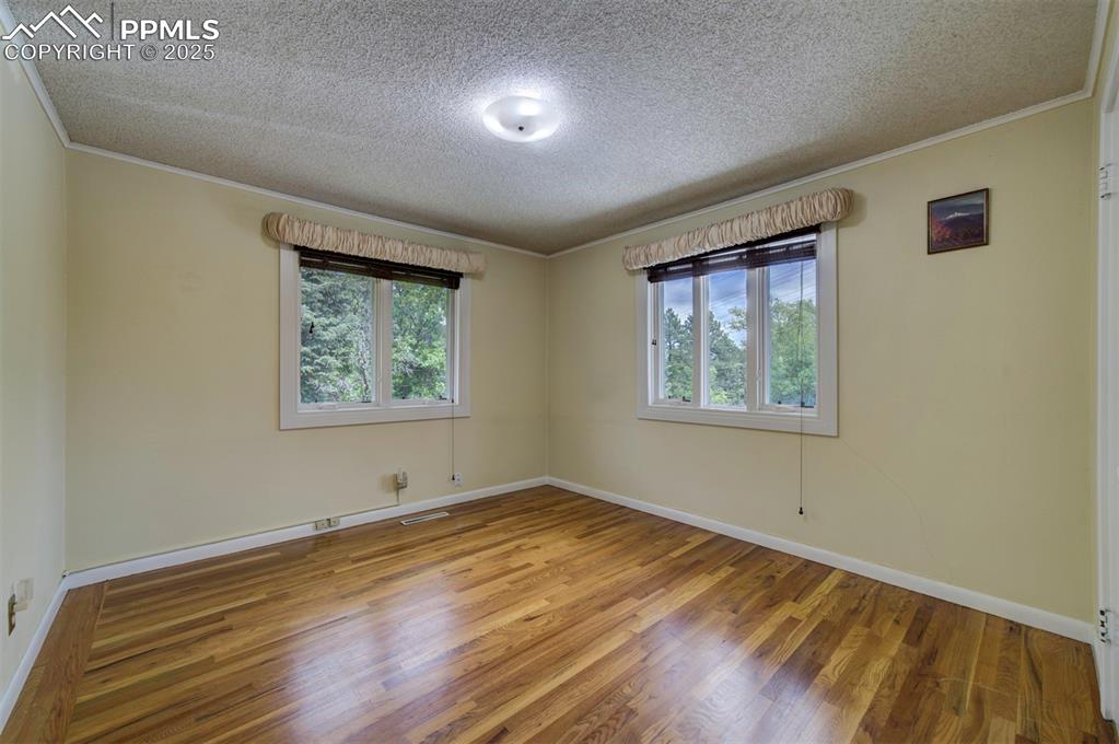 Image 25 of 49: Empty room with ornamental molding, a textured ceiling, wood finished floor