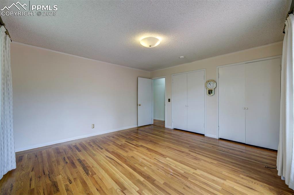Image 30 of 49: Unfurnished bedroom with a textured ceiling, multiple closets, light wood f