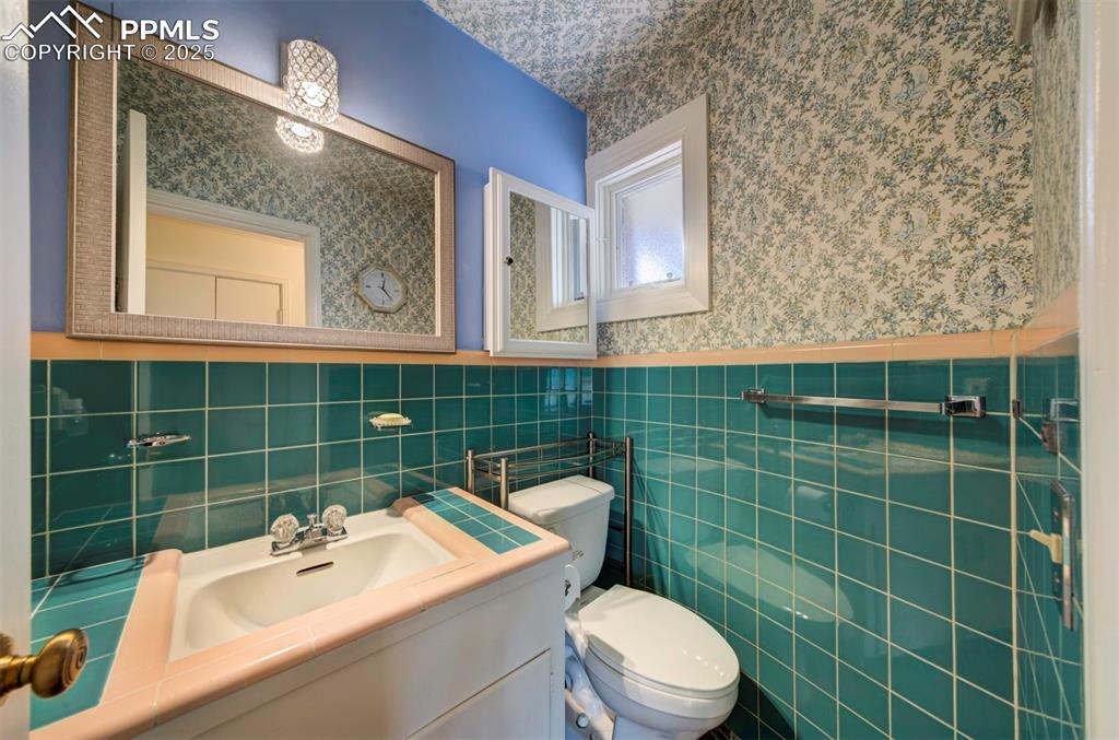 Image 35 of 49: Bathroom featuring wallpapered walls, toilet, wainscoting, vanity, and tile