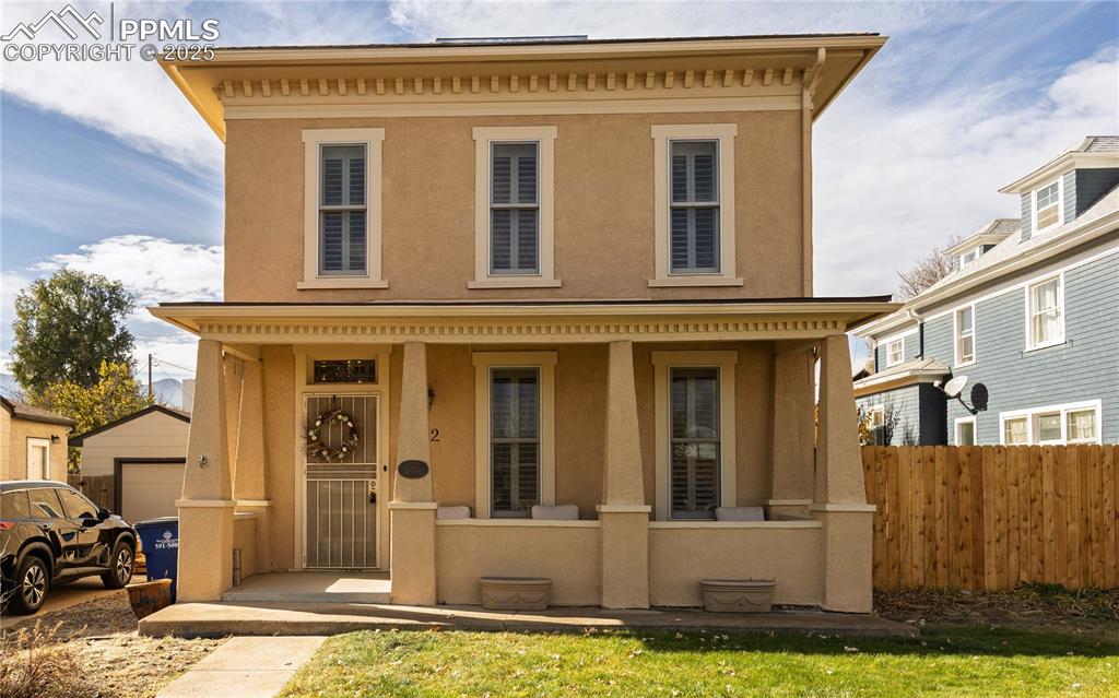 Caption: Italianate home featuring covered porch, stucco siding, and a detached garage