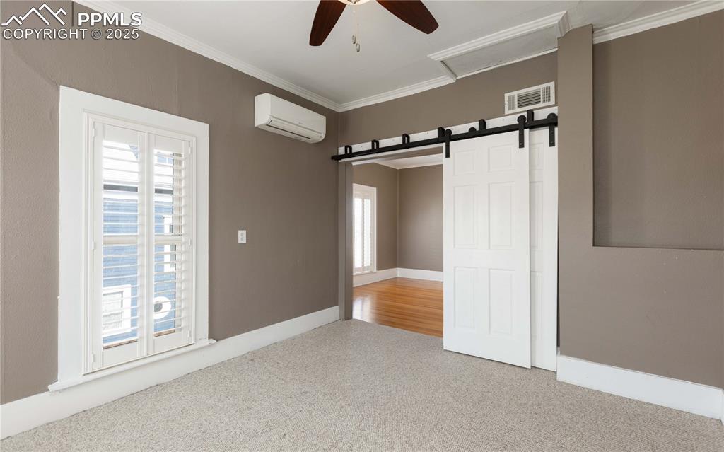 Image 19 of 31: Unfurnished room with ceiling fan, carpet, a barn door, ornamental molding,