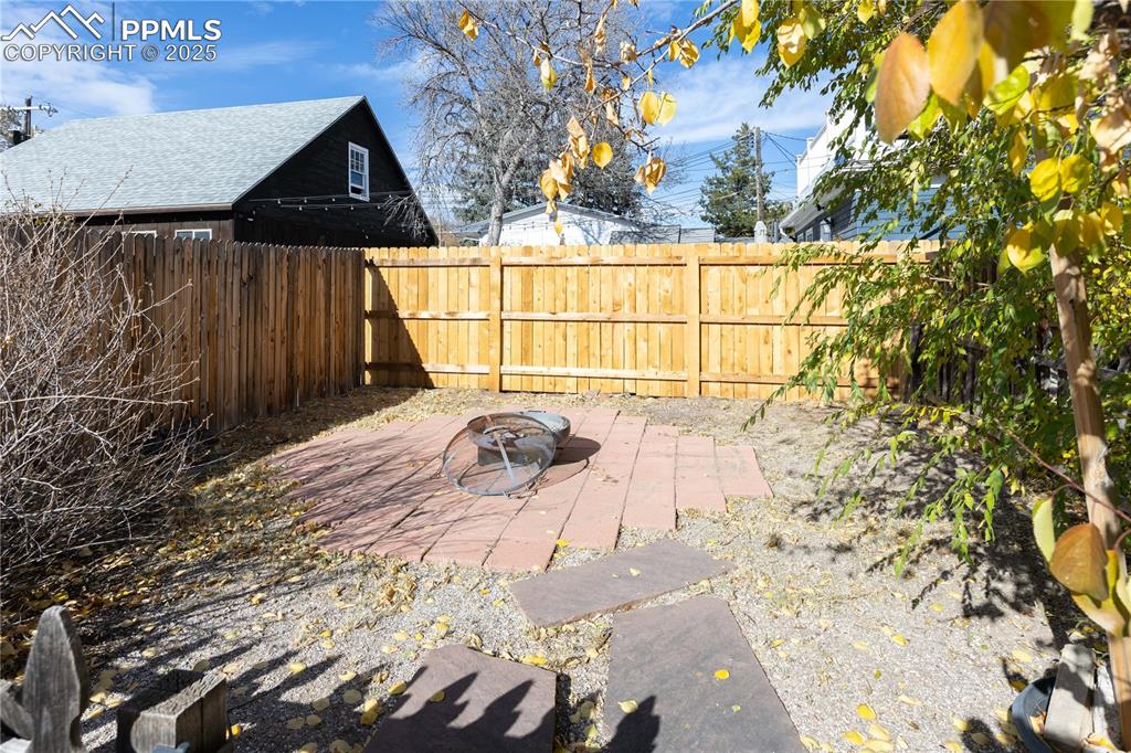 Image 29 of 31: Fenced backyard with an outdoor fire pit and a patio