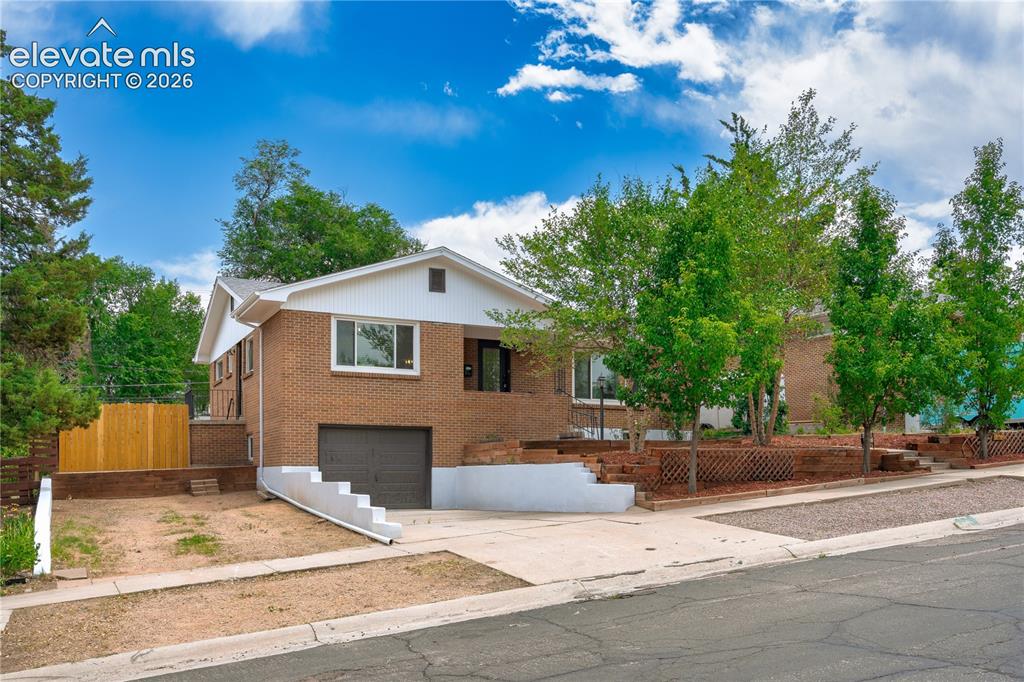 Image 25 of 38: Brick-clad home featuring a front-facing garage with a dark door, white-tri