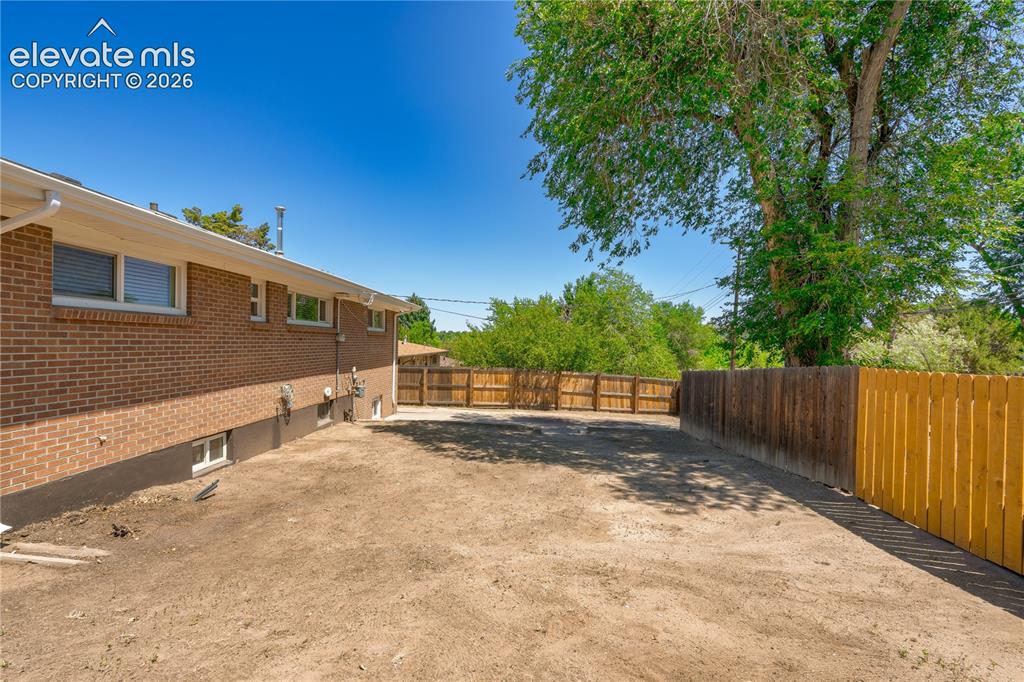 Image 25 of 36: Spacious backyard featuring a full privacy fence, mature trees, and a red b