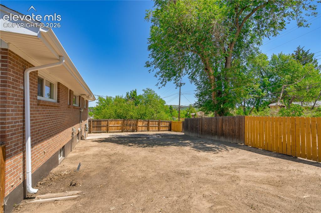 Image 26 of 36: Expansive rear yard featuring a brick exterior, multiple windows, and parti