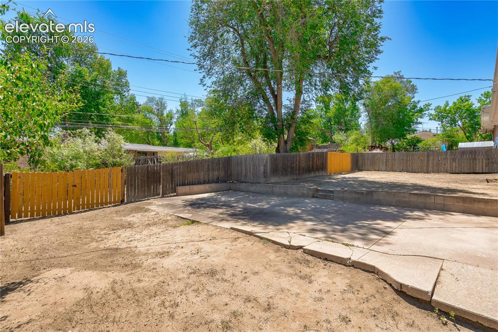 Image 29 of 36: Rear yard with concrete patio, wood fencing, and a tiered retaining wall