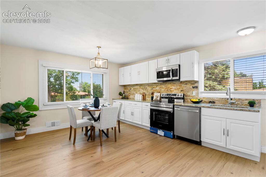 Image 3 of 36: Bright kitchen featuring wood-finish flooring, white cabinetry, integrated