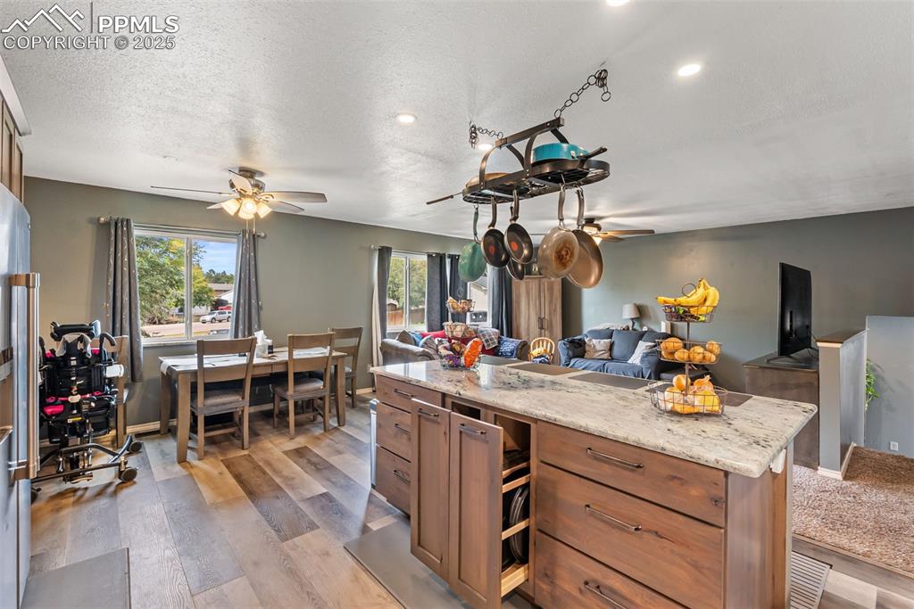 Image 12 of 50: Kitchen with light wood-style floors, brown cabinetry, light stone countert