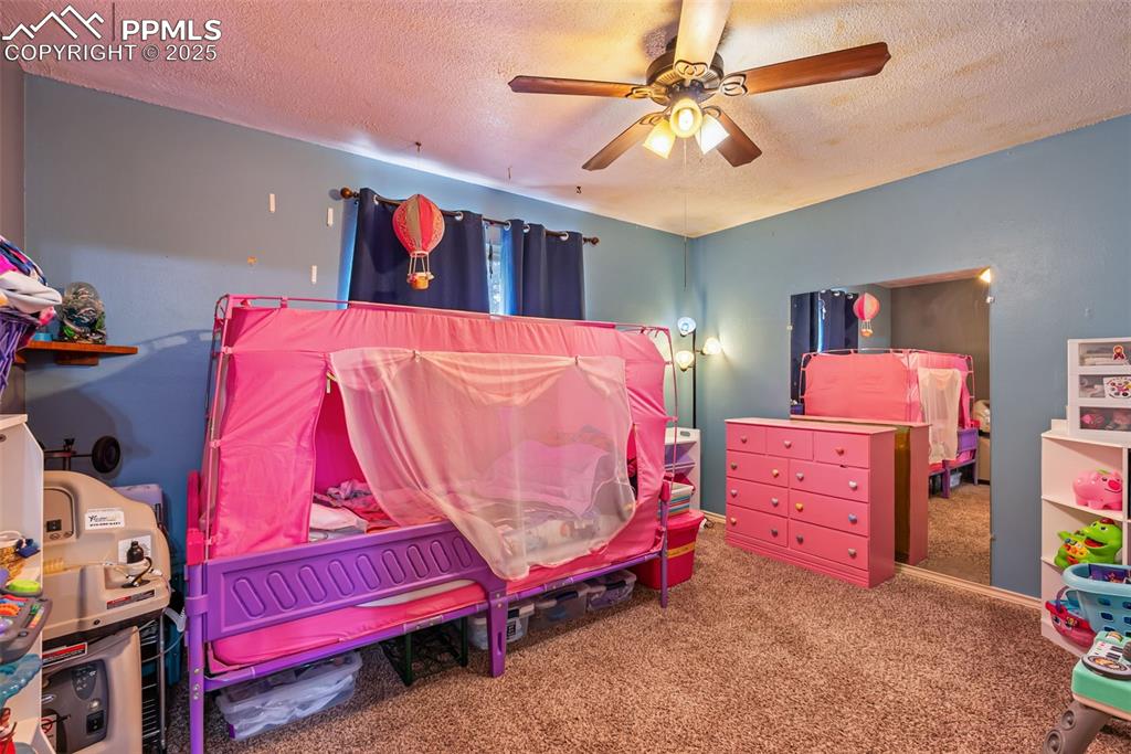 Image 23 of 50: Carpeted bedroom with a textured ceiling and ceiling fan