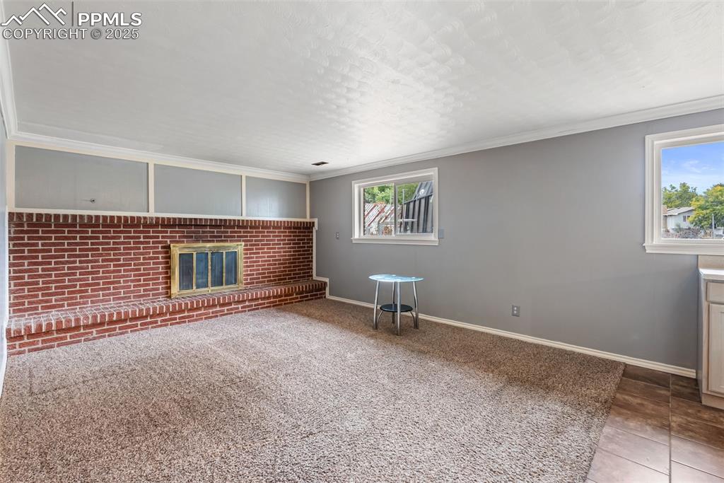 Image 29 of 50: Unfurnished living room with crown molding, a fireplace, carpet floors, bri
