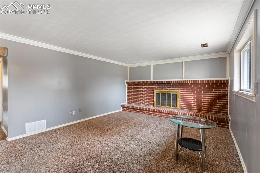 Image 30 of 50: Unfurnished living room with crown molding, carpet floors, and a fireplace