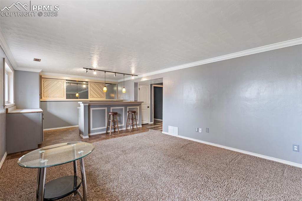 Image 31 of 50: Unfurnished living room with crown molding, carpet floors, a dry bar, and r