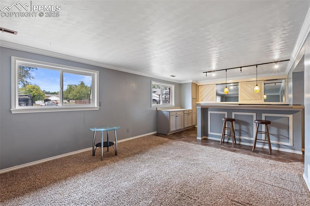 Image 32 of 50: Unfurnished living room featuring dark colored carpet, ornamental molding,