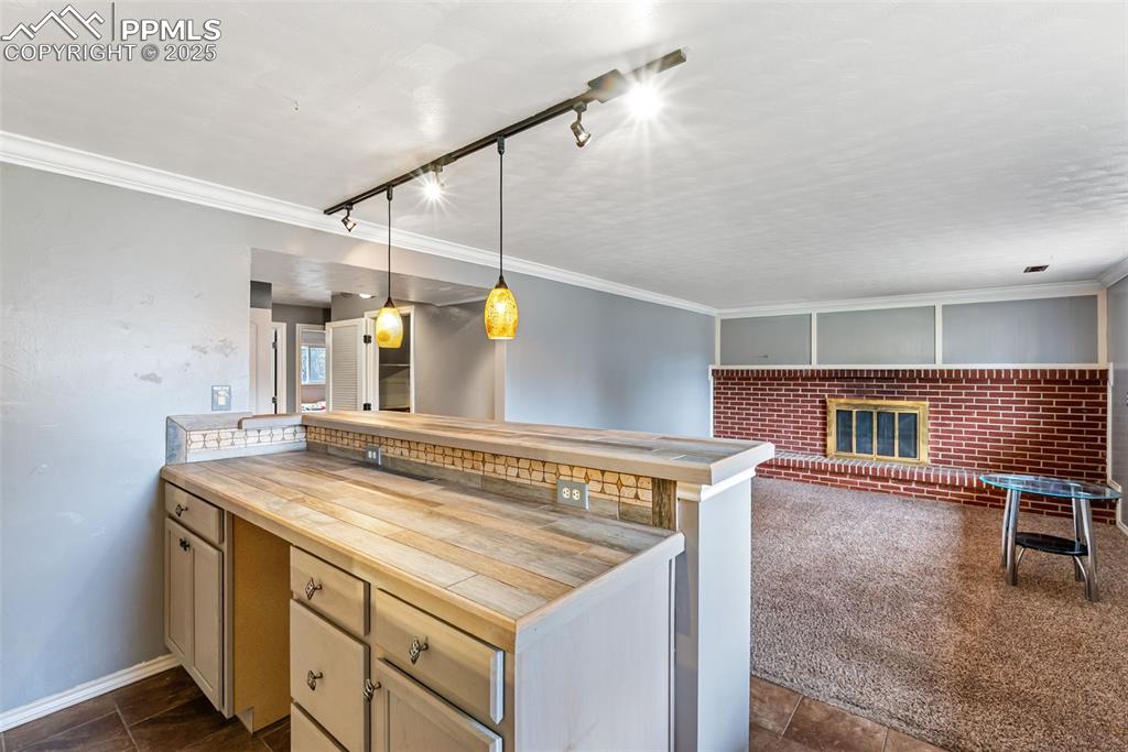 Image 34 of 50: Kitchen with crown molding, track lighting, a brick fireplace, hanging ligh