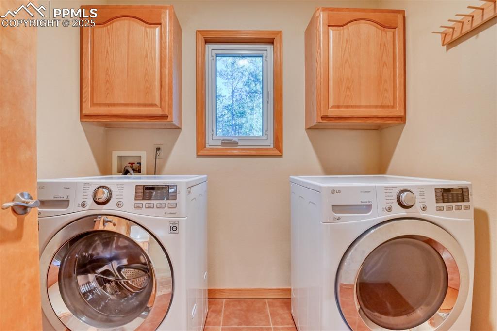 Image 14 of 23: Washroom with tile patterned floors, separate washer and dryer, and cabinet