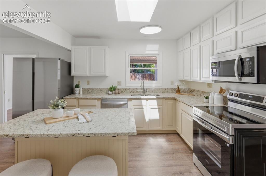 Image 11 of 34: Kitchen featuring a skylight, recessed lighting, white upper cabinetry, lig