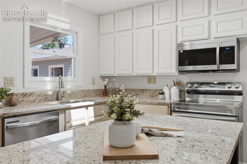 Image 12 of 34: White cabinetry, stainless steel appliances, stainless steel sink, light-to