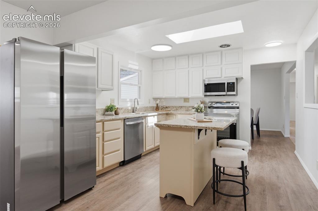 Image 13 of 34: Kitchen featuring stainless steel appliances, wood-finish flooring, white u