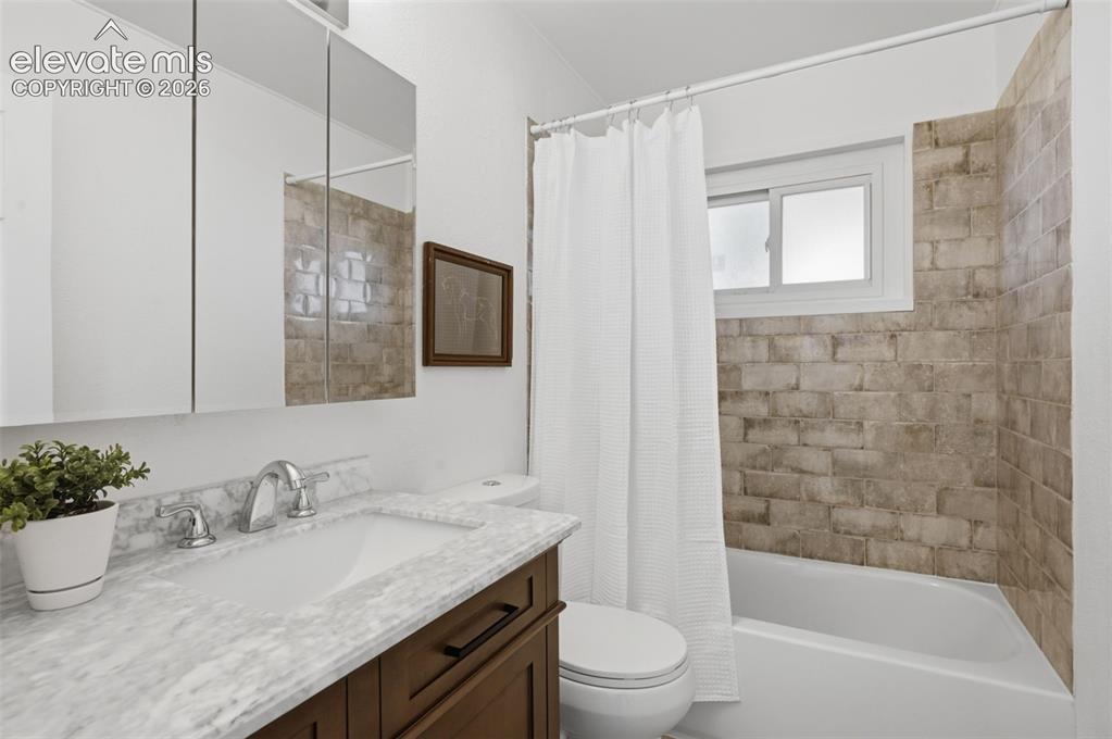Image 25 of 34: Bathroom featuring a wood-finish vanity, integrated white sink, stone-finis