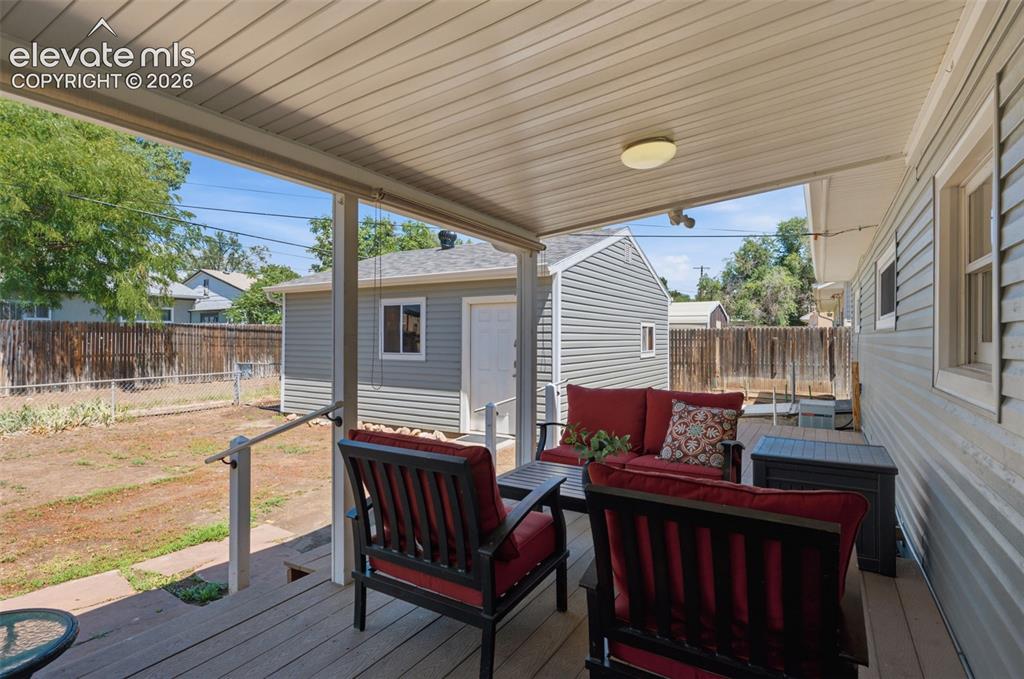 Image 26 of 34: Covered outdoor deck with a ceiling-mounted light fixture, leading to a fen