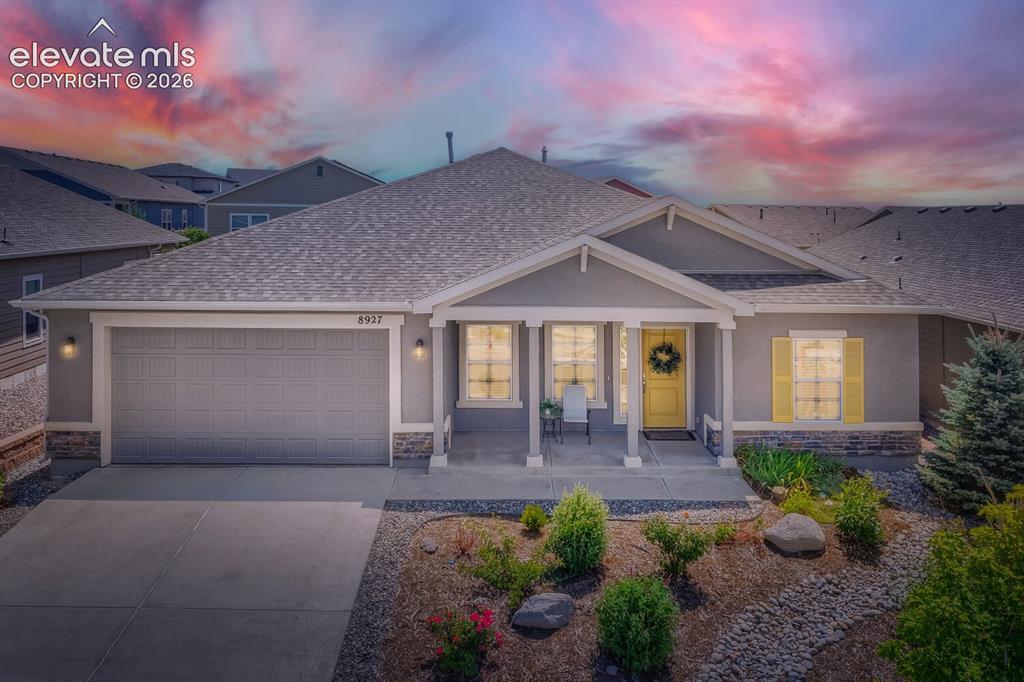 Caption: Ranch-style exterior featuring a covered front porch with columns, a two-car garage, and a landscape