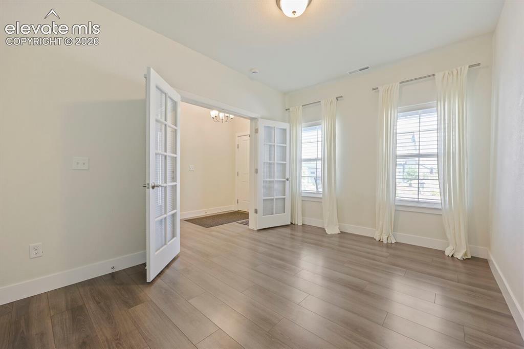Image 13 of 45: Room featuring French doors, wood-finish flooring, two windows with blinds,