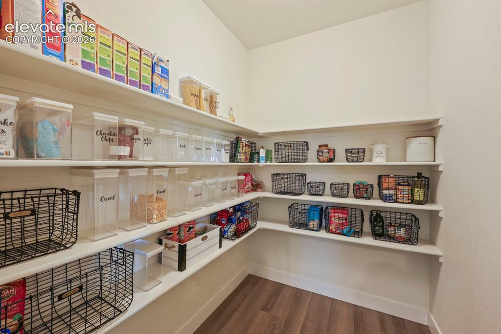 Image 16 of 45: Spacious walk-in pantry featuring multiple levels of white shelving, wood-f