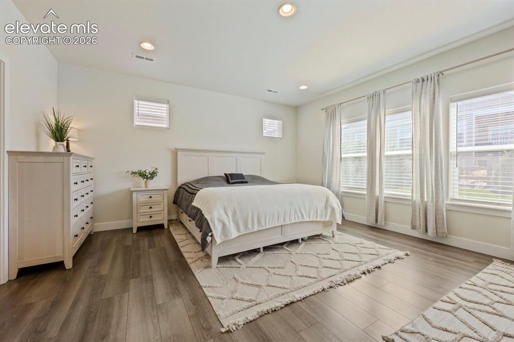 Image 18 of 45: Spacious primary bedroom featuring wood-finish flooring and recessed lighti
