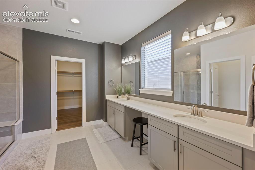 Image 21 of 45: Generously sized primary bathroom features a dual vanity with light gray ca