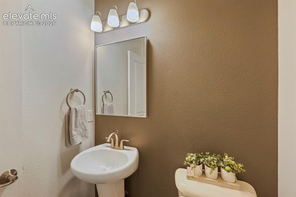 Image 28 of 45: Pedestal sink with brass-finish faucet, framed mirror, and a three-light va