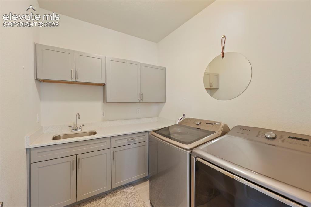 Image 29 of 45: Spacious utility room featuring white walls, light gray cabinetry, a stainl