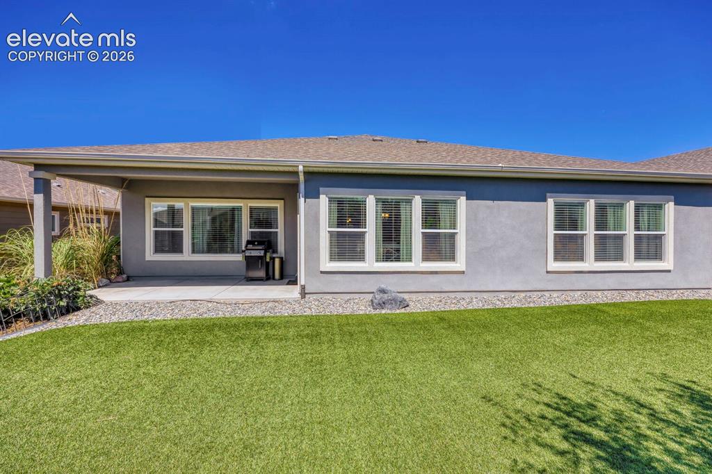 Image 41 of 45: Expansive artificial turf lawn with a covered patio featuring stucco column