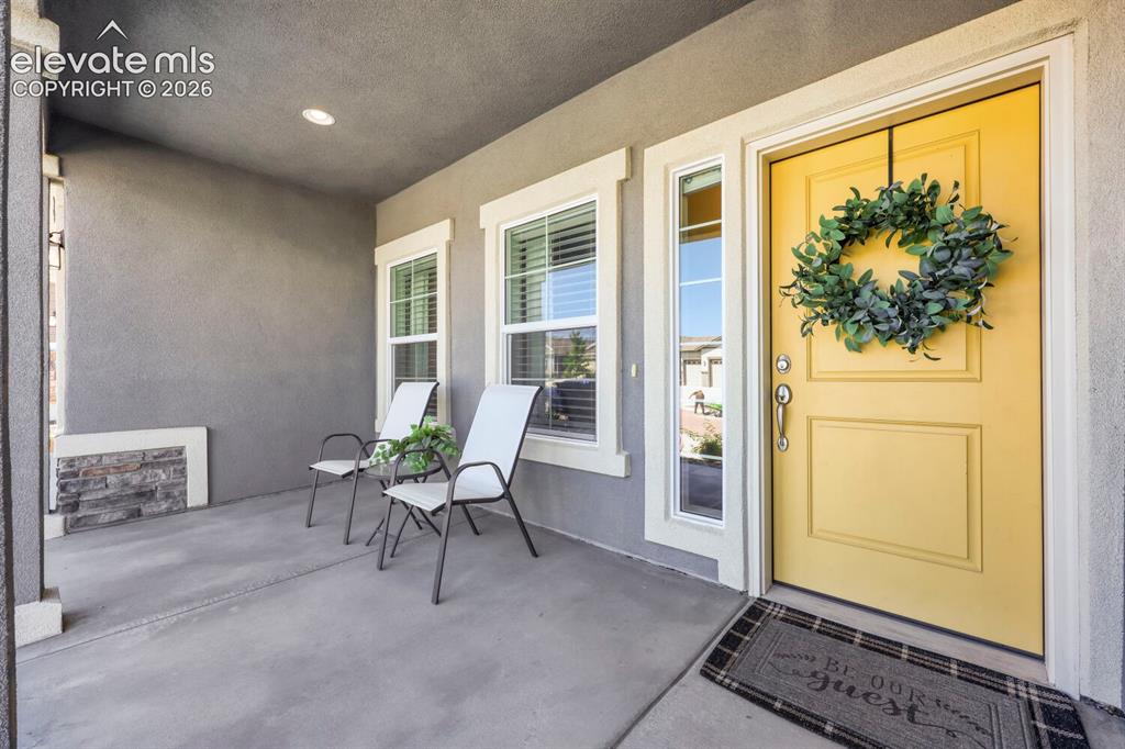 Image 7 of 45: Covered front porch featuring a striking yellow entry door with sidelight w
