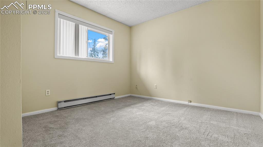Image 12 of 25: Empty room featuring light carpet, a baseboard heating unit, and a textured
