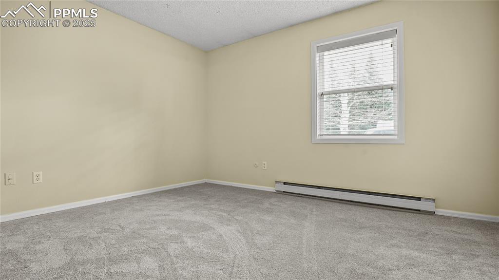 Image 14 of 25: Spare room featuring a baseboard radiator, a textured ceiling, and carpet f
