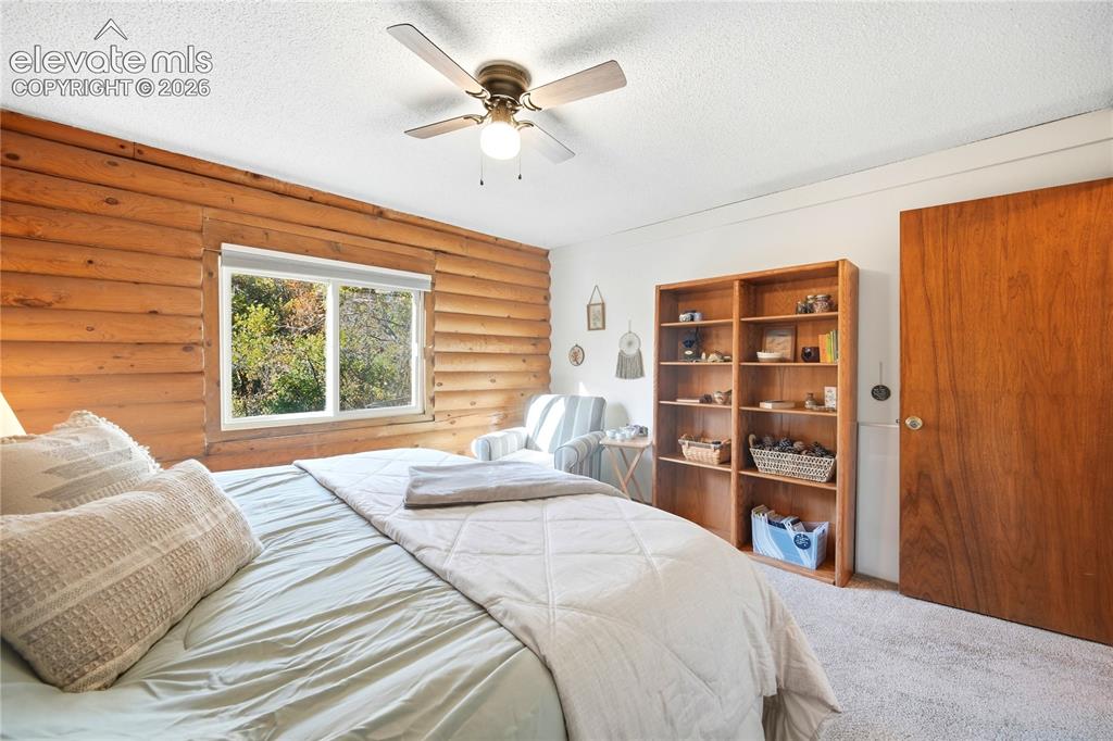 Image 15 of 34: Wood-paneled accent wall, built-in shelving, ceiling fan, and window with n