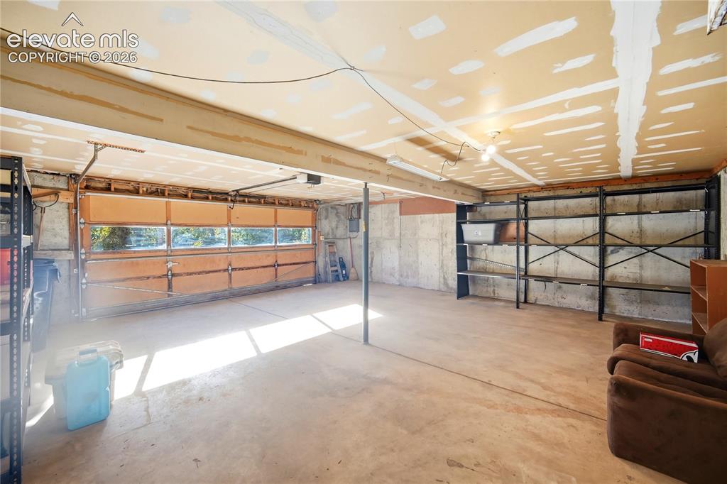 Image 21 of 34: Spacious garage with concrete flooring, wood-paneled garage door with windo