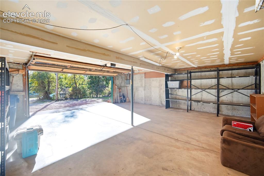 Image 22 of 34: Spacious garage featuring concrete flooring and exposed ceiling beams
